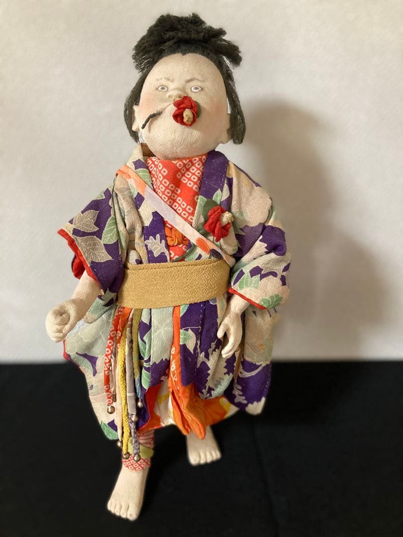 古い縮緬の着物を重ね着、手作りの太鼓を肩からさげています。口に縮緬の椿